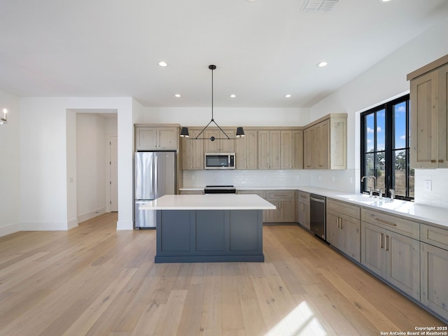 kitchen with sink, light hardwood / wood-style flooring, appliances with stainless steel finishes, decorative light fixtures, and a kitchen island