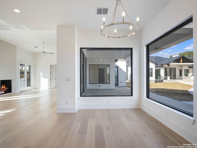 interior space with ceiling fan with notable chandelier, a fireplace, and light hardwood / wood-style flooring