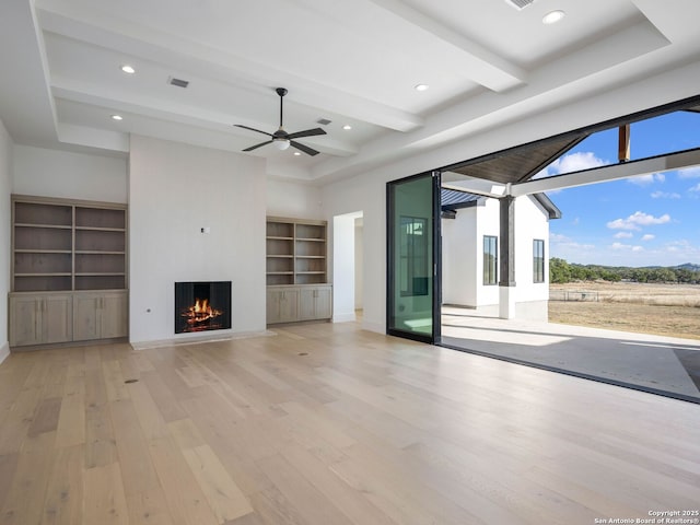 unfurnished living room with ceiling fan, built in features, beamed ceiling, a towering ceiling, and light wood-type flooring