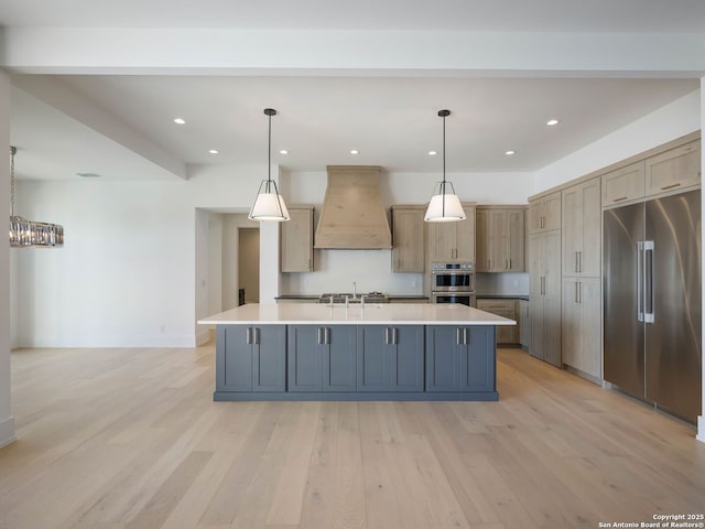 kitchen featuring a center island with sink, custom exhaust hood, hanging light fixtures, and appliances with stainless steel finishes