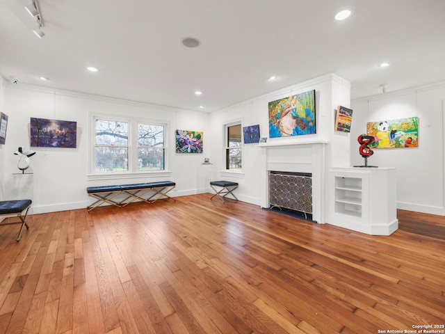 unfurnished living room featuring hardwood / wood-style floors, track lighting, and ornamental molding