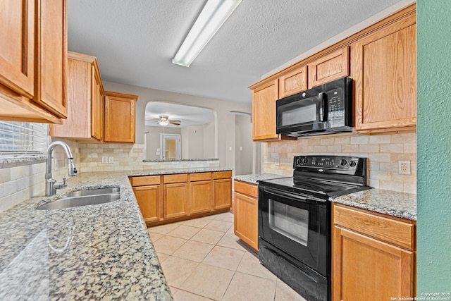 kitchen featuring decorative backsplash, light stone countertops, sink, black appliances, and light tile patterned floors