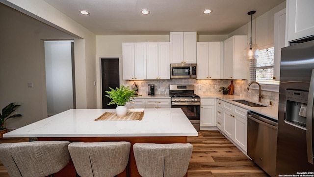 kitchen with appliances with stainless steel finishes, a kitchen island, sink, pendant lighting, and white cabinetry