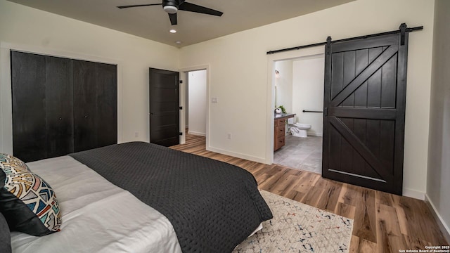 bedroom with ceiling fan, a barn door, ensuite bathroom, a closet, and hardwood / wood-style flooring