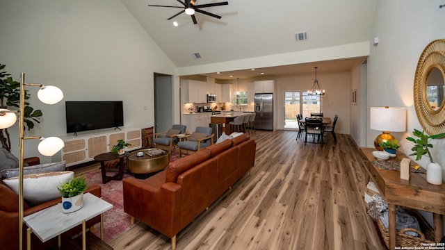 living room featuring ceiling fan with notable chandelier, light hardwood / wood-style flooring, and high vaulted ceiling