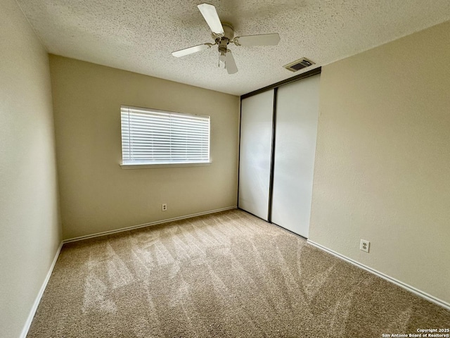 unfurnished bedroom with a textured ceiling, a closet, ceiling fan, and light colored carpet