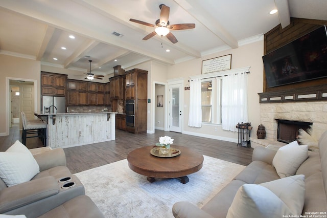 living room featuring ceiling fan, beam ceiling, a stone fireplace, and wood-type flooring