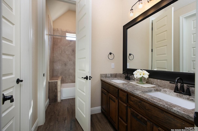 bathroom featuring vanity, wood-type flooring, tiled shower / bath combo, and vaulted ceiling