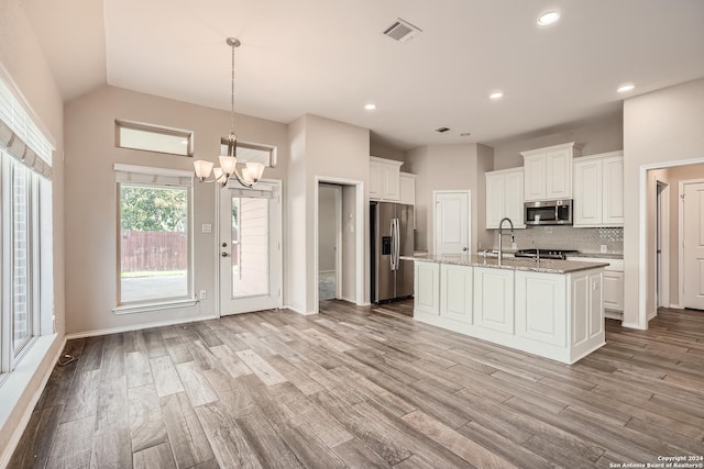 kitchen with a kitchen island with sink, white cabinets, vaulted ceiling, and appliances with stainless steel finishes