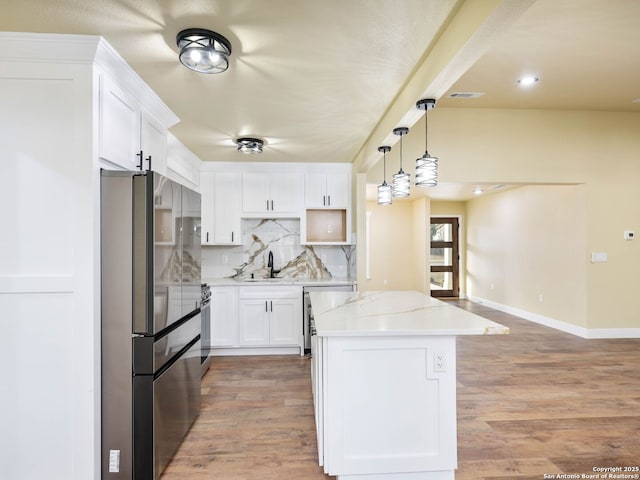 kitchen with stainless steel refrigerator, white cabinetry, light stone countertops, backsplash, and hardwood / wood-style floors