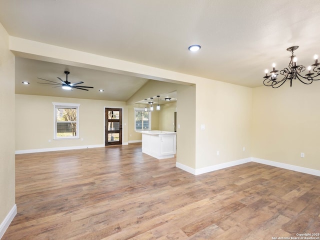 unfurnished living room with ceiling fan with notable chandelier, light wood-type flooring, and lofted ceiling