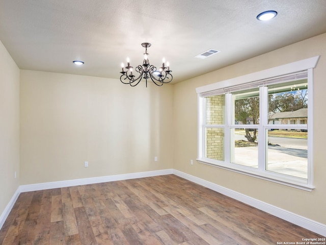 spare room with hardwood / wood-style flooring and an inviting chandelier