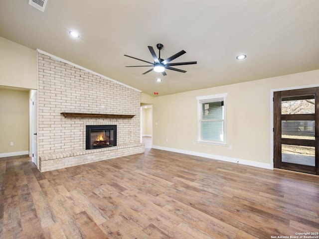 unfurnished living room featuring ceiling fan, hardwood / wood-style floors, lofted ceiling, and a brick fireplace