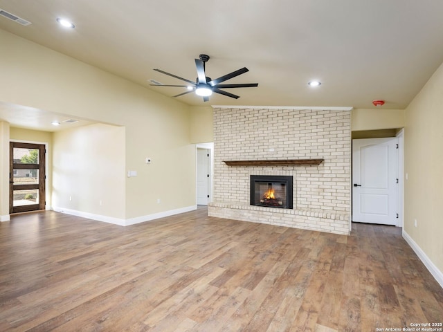 unfurnished living room featuring lofted ceiling, ceiling fan, wood-type flooring, and a brick fireplace