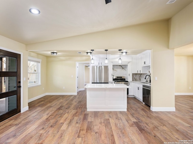 kitchen featuring white cabinetry, hanging light fixtures, stainless steel appliances, backsplash, and a kitchen island