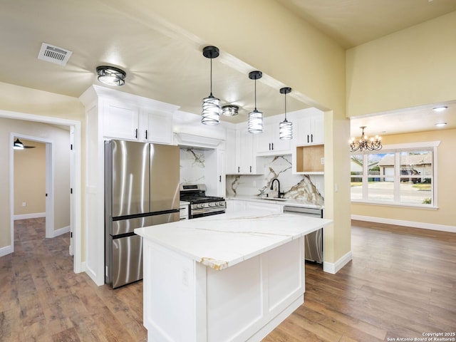 kitchen with white cabinets, light stone countertops, a kitchen island, stainless steel appliances, and a chandelier