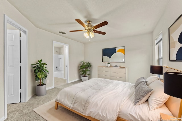 bedroom with a textured ceiling, ensuite bathroom, ceiling fan, and light colored carpet