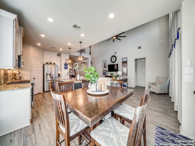 dining area with sink, ceiling fan, a high ceiling, and light hardwood / wood-style flooring