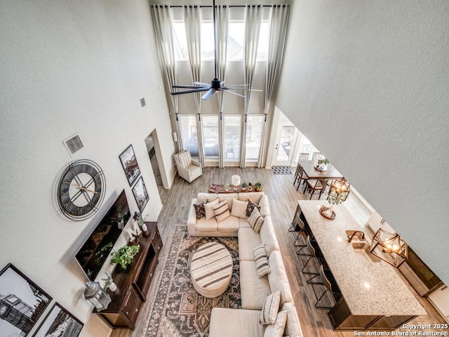 living room with ceiling fan, wood-type flooring, a high end fireplace, and a towering ceiling