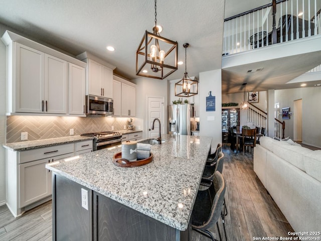 kitchen featuring decorative backsplash, white cabinets, decorative light fixtures, an island with sink, and stainless steel appliances