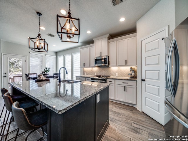 kitchen featuring a center island with sink, white cabinetry, pendant lighting, and appliances with stainless steel finishes