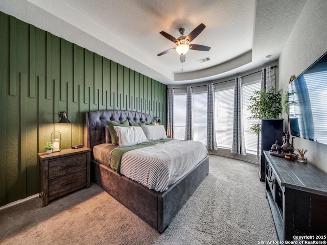 bedroom with ceiling fan, a raised ceiling, a textured ceiling, and carpet flooring