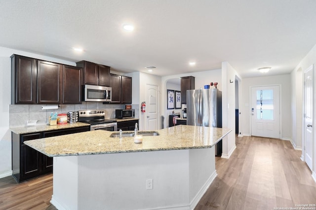 kitchen with a center island with sink, backsplash, dark brown cabinets, and stainless steel appliances