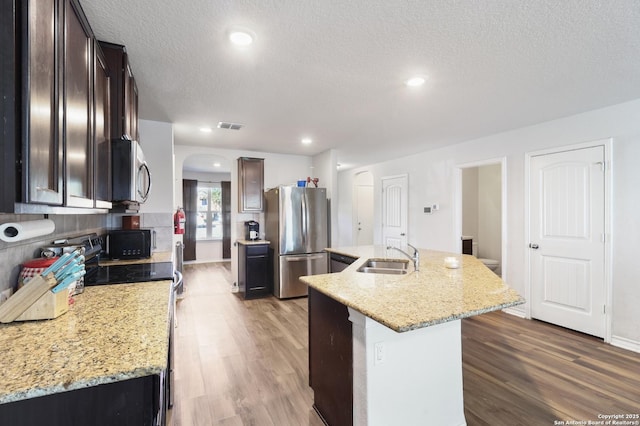 kitchen with light stone countertops, appliances with stainless steel finishes, sink, and an island with sink