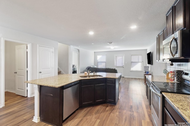 kitchen featuring appliances with stainless steel finishes, dark brown cabinets, a kitchen island with sink, sink, and hardwood / wood-style flooring