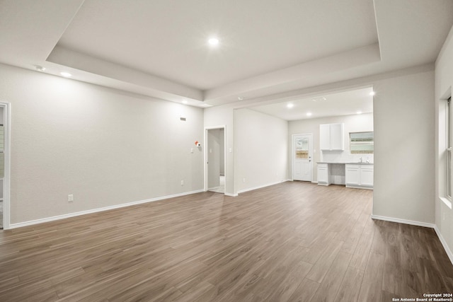 unfurnished living room with sink, a tray ceiling, and hardwood / wood-style flooring