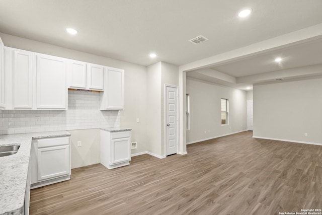 kitchen featuring decorative backsplash, white cabinetry, light hardwood / wood-style floors, and light stone counters