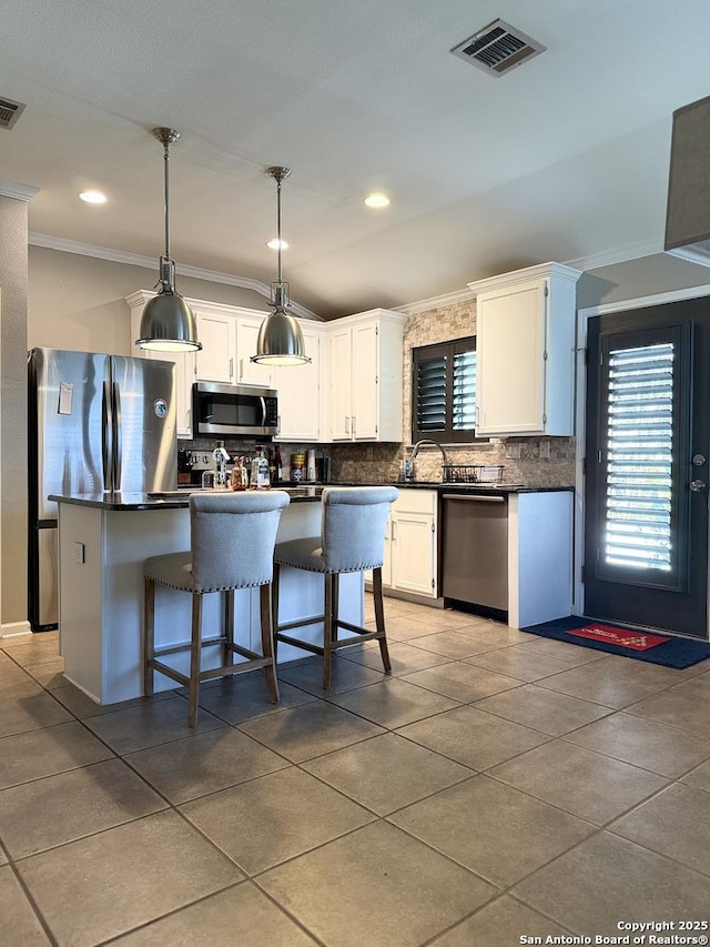 kitchen with appliances with stainless steel finishes, backsplash, a kitchen island, pendant lighting, and white cabinetry