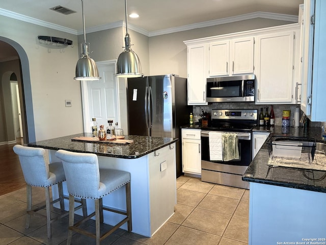 kitchen featuring a center island, hanging light fixtures, stainless steel appliances, dark stone counters, and white cabinets