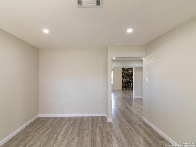 unfurnished room with a stone fireplace and light wood-type flooring