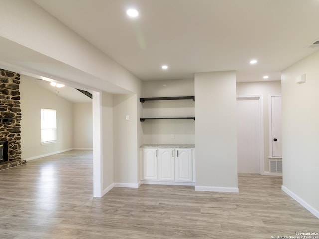 unfurnished living room featuring lofted ceiling, light hardwood / wood-style flooring, ceiling fan, and a stone fireplace