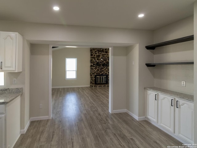 kitchen featuring light stone countertops, white cabinetry, a fireplace, and light hardwood / wood-style flooring