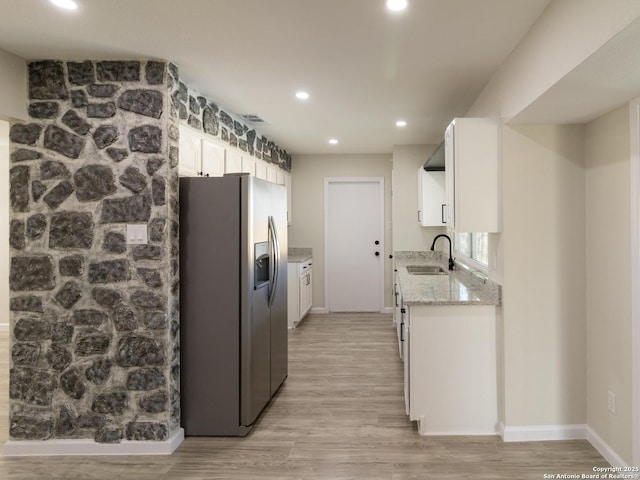 kitchen with sink, light stone counters, stainless steel fridge, light hardwood / wood-style floors, and white cabinets