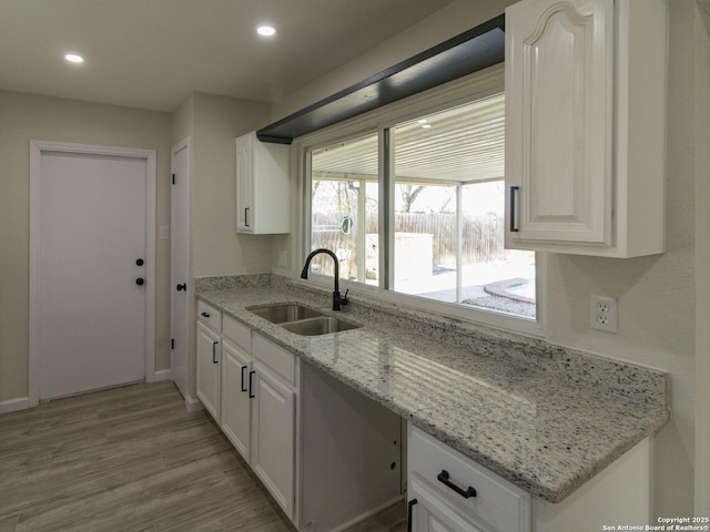 kitchen featuring white cabinetry, sink, light stone countertops, and light wood-type flooring