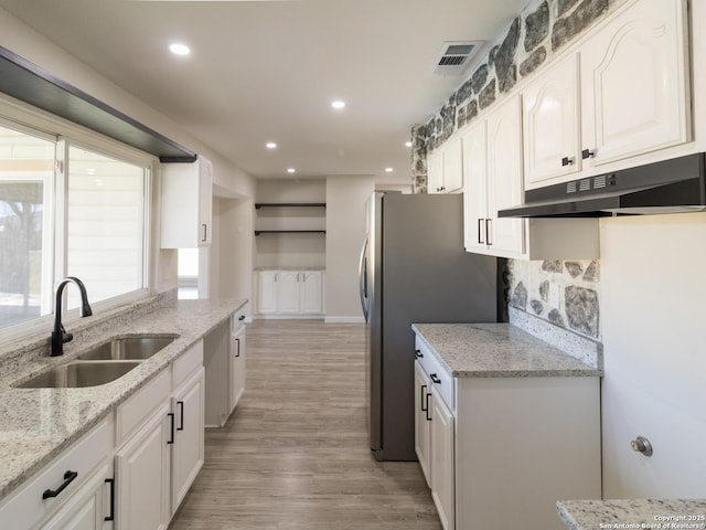 kitchen with light stone counters, white cabinetry, sink, and light hardwood / wood-style flooring