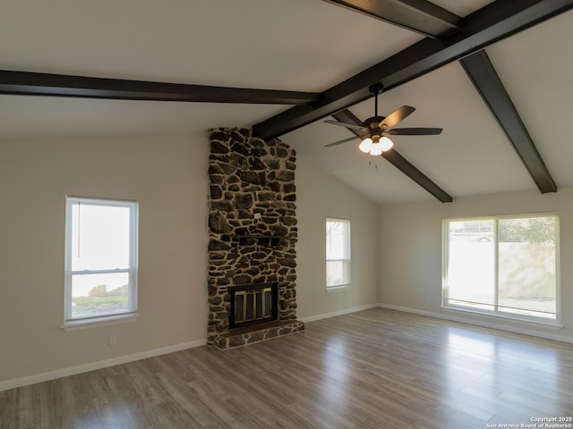 unfurnished living room featuring lofted ceiling with beams, a stone fireplace, ceiling fan, a healthy amount of sunlight, and wood-type flooring