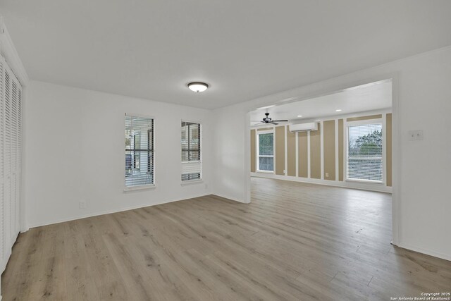 empty room with a wall unit AC, ceiling fan, and light wood-type flooring