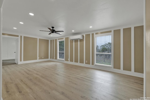 empty room with a wall mounted air conditioner, light wood-type flooring, and ceiling fan