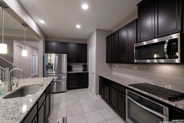 kitchen featuring light stone counters, stainless steel appliances, a sink, and decorative light fixtures