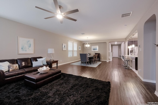 living area with dark wood-style floors, arched walkways, visible vents, and baseboards