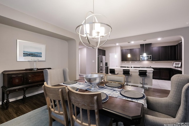 dining room featuring light wood-style floors, baseboards, arched walkways, and a notable chandelier