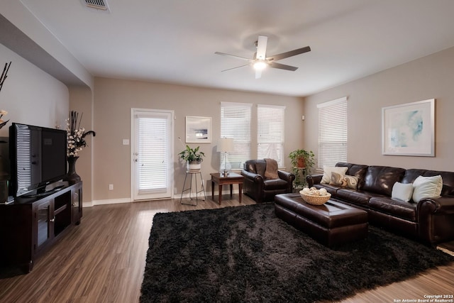 living area featuring dark wood-type flooring, a healthy amount of sunlight, baseboards, and a ceiling fan