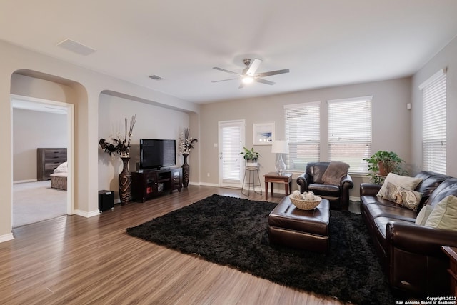 living area featuring baseboards, ceiling fan, arched walkways, and wood finished floors