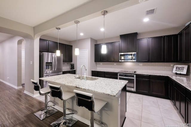 kitchen featuring arched walkways, light stone counters, decorative light fixtures, stainless steel appliances, and a sink