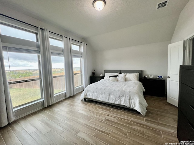 bedroom with a textured ceiling, light hardwood / wood-style floors, multiple windows, and vaulted ceiling