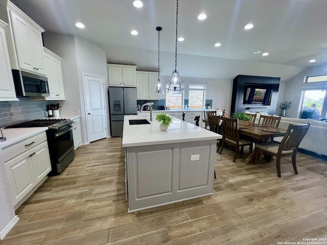 kitchen with hanging light fixtures, stainless steel appliances, tasteful backsplash, a center island with sink, and white cabinets